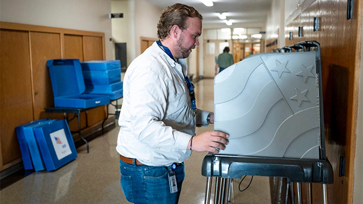 Aiden Stahl, becario de la división electoral de la oficina del secretario del condado de Kenosha, instala cabinas de votación en un pasillo del Edificio Municipal de Kenosha para preparar la votación anticipada en persona en Kenosha, Wisconsin, el 21 de octubre de 2024. (Scott Olson/Getty Images)