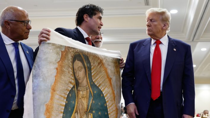 El candidato presidencial republicano, el expresidente de los Estados Unidos Donald Trump, recibe una obra de arte del actor mexicano Eduardo Verástegui (centro) mientras participa en una mesa redonda en la Cumbre Latina celebrada en el Trump National Doral Golf Club el 22 de octubre de 2024 en Doral, Florida. (Anna Moneymaker/Getty Images)