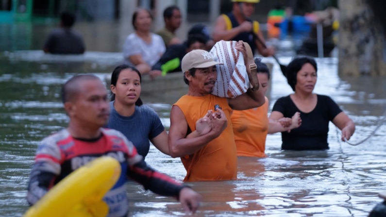 Residentes con sus pertenencias vadean una calle inundada por las fuertes lluvias provocadas por la tormenta tropical Trami en Naga City, provincia de Camarines Sur (Filipinas), el 24 de octubre de 2024. (Zalrian Sayat/AFP vía Getty Images)