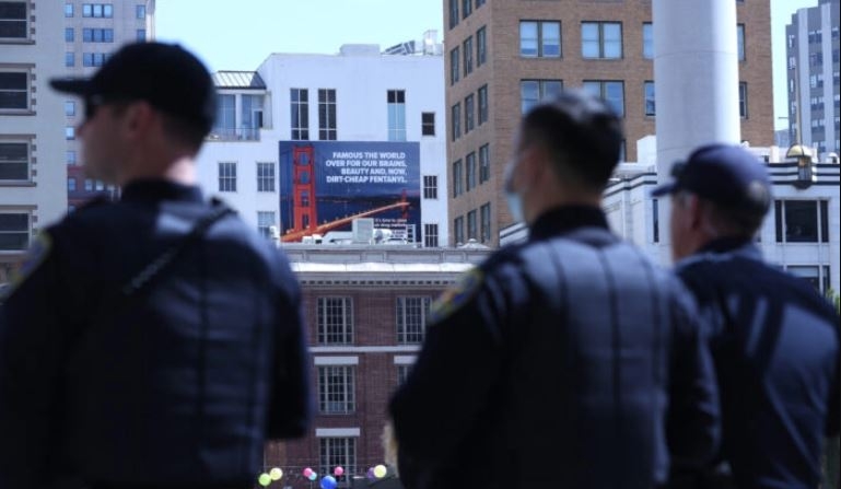 Agentes de policía de San Francisco observan cerca de una valla publicitaria que advierte contra el fentanilo en San Francisco el 4 de abril de 2022. (Justin Sullivan/Getty Images)