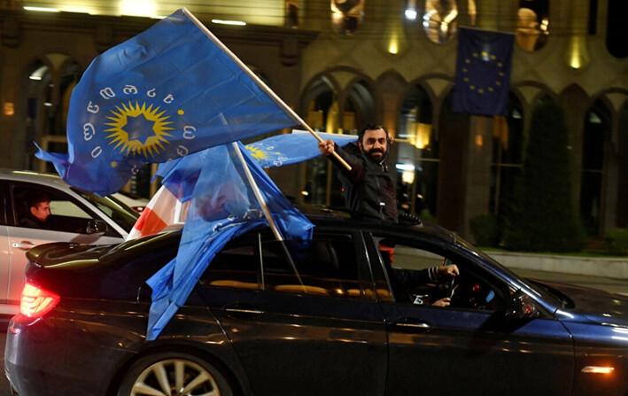 Un simpatizante del partido Sueño Georgiano ondea las banderas del partido desde un automóvil después del anuncio de los resultados de las encuestas a boca de urna en las elecciones parlamentarias, en Tbilisi, Georgia, el 26 de octubre de 2024. (Zurab Javakhadze/Reuters)