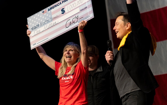 Elon Musk, fundador de SpaceX y Tesla, le entrega a Kristine Fishell un cheque de un millón de dólares durante un foro abierto en el Teatro Roxian, en Pittsburgh, el 20 de octubre de 2024. (Michael Swensen/Getty Images)