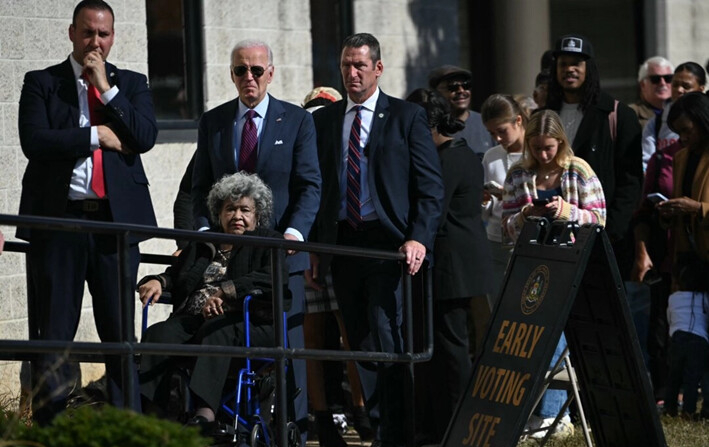 El presidente Joe Biden empuja a una mujer en silla de ruedas mientras los votantes esperan en fila afuera de un centro de votación en New Castle, Delaware, el 28 de octubre de 2024. (Andrew Caballero-Reynolds/AFP/Getty Images)