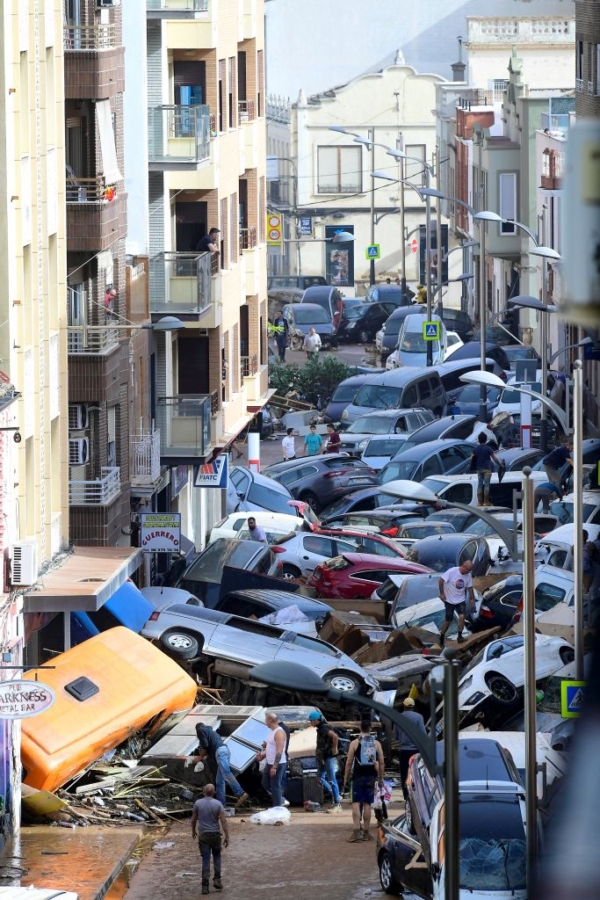 Peatones junto a coches apilados tras las inundaciones mortales en Sedavi, al sur de Valencia, este de España, el 30 de octubre de 202 (Jose Jordan / AFPvia Getty Images)