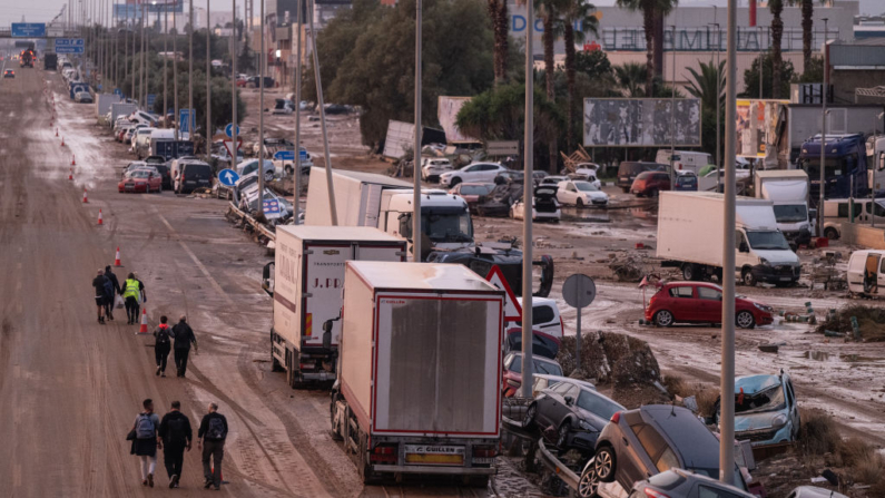 La gente camina junto a automóviles y camiones que se encontraban entre los escombros arrastrados por las recientes inundaciones repentinas a lo largo de la autopista V-31 cerca del municipio de Massanassa el 1 de noviembre de 2024 en las afueras de Valencia, España. (David Ramos/Getty Images)