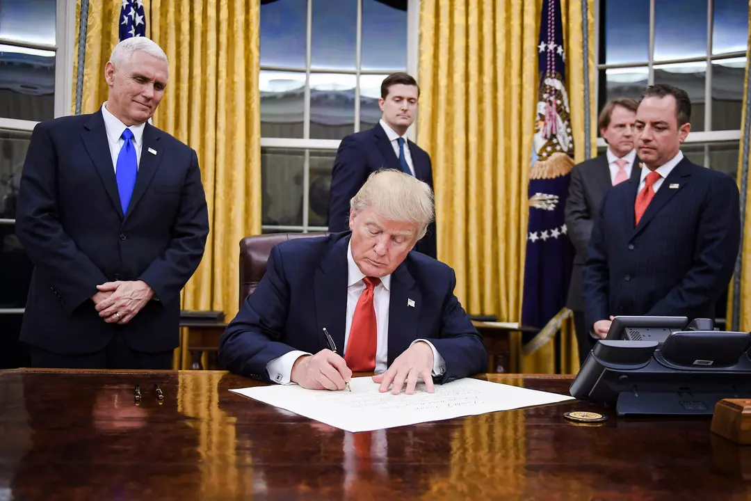 El presidente Donald Trump firma una orden ejecutiva mientras el vicepresidente Mike Pence y el jefe de gabinete Reince Priebus observan en la Casa Blanca el 20 de enero de 2017. (Jim Watson/AFP vía Getty Images)