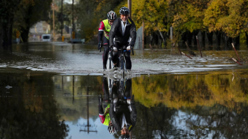 Dave Edmonds (d) y Mike Raasch montan en bicicleta en una carretera inundada en Windsor, California, el 23 de noviembre de 2024. (Godofredo A. Vásquez/Foto AP)
