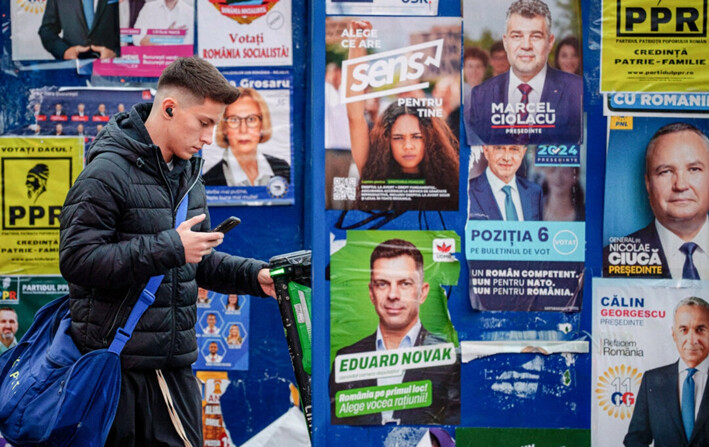 Un joven camina con su teléfono celular frente a los carteles electorales de los principales candidatos presidenciales en Bucarest, Rumania, el 22 de noviembre de 2024. (Andreea Alexandru/AP)