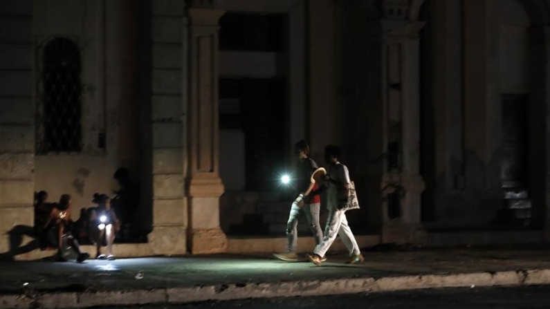 Personas caminan por una calle sin iluminación auxiliándose con la luz de su celular durante un apagón, el 18 de agosto de 2022, en La Habana (Cuba). EFE/Ernesto Mastrascusa