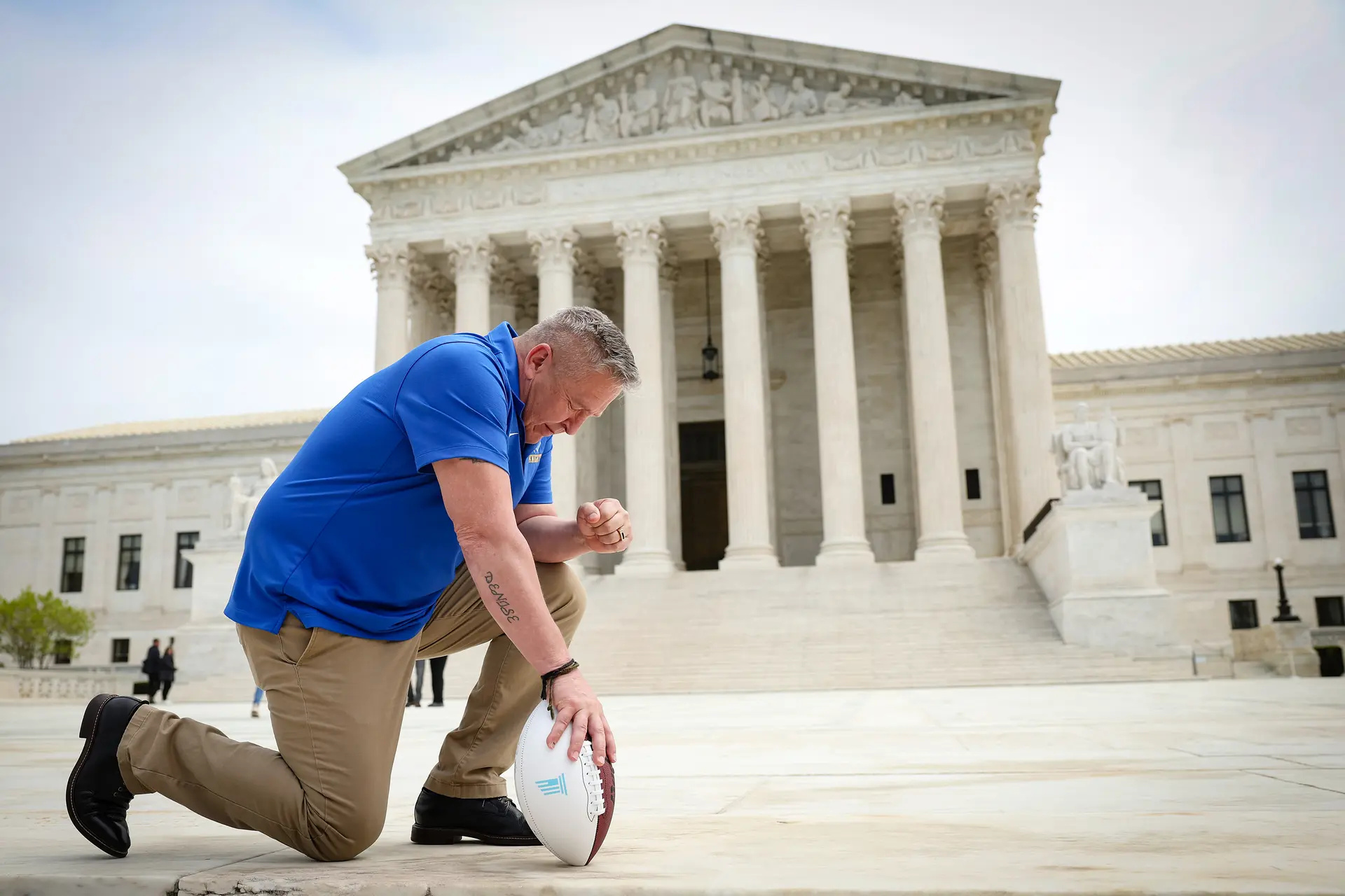 El exentrenador asistente de fútbol americano de Bremerton High School, Joe Kennedy, se arrodilla ante la Corte Suprema de EE. UU. después de que su caso legal, Kennedy contra el Distrito Escolar de Bremerton, fuera argumentado ante el tribunal, en Washington el 25 de abril de 2022. Kennedy fue despedido por las autoridades de la escuela pública de Bremerton en 2015 tras negarse a dejar de rezar en el campo después de los partidos de fútbol. (Win McNamee/Getty Images)