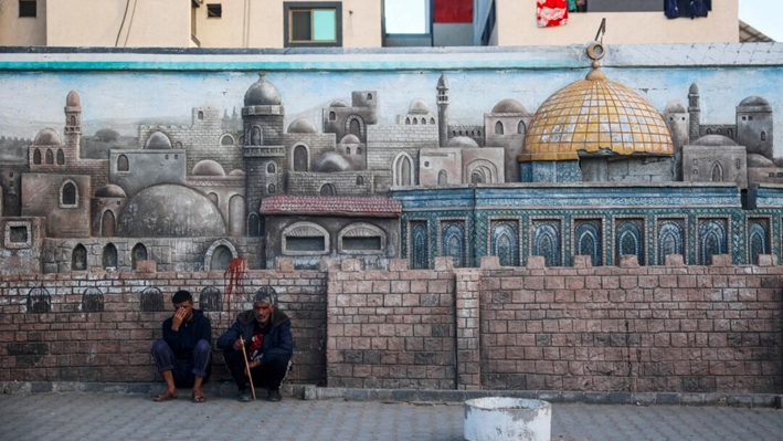 Unos hombres se agachan junto a un muro que muestra un relieve que representa la Ciudad Vieja de Jerusalén y su complejo de la mezquita Al-Aqsa, en Deir el-Balah, en el centro de la Franja de Gaza, el 14 de diciembre de 2024, mientras continúa la guerra entre Israel y el grupo palestino Hamás. (Eyad Baba/AFP vía Getty Images)