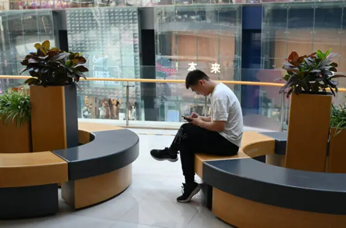 Un hombre consulta su teléfono mientras descansa en un centro comercial de Beijing, el 18 de julio de 2023. (Greg Baker/AFP vía Getty Images)