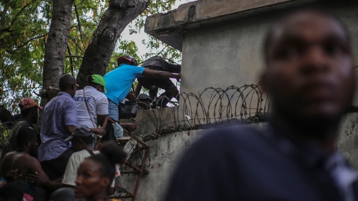 Periodistas trepan un muro para protegerse de los disparos, luego de que bandas armadas les dispararan en el Hospital General de Puerto Príncipe, Haití, el 24 de diciembre de 2024. (Jean Feguens Regala/AP Photo)