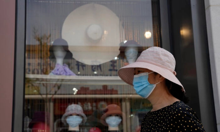 Una mujer con mascarilla pasa junto a cabezas de maniquí con mascarillas en una sombrerería de Beijing el 9 de septiembre de 2022. (Ng Han Guan/Foto AP)