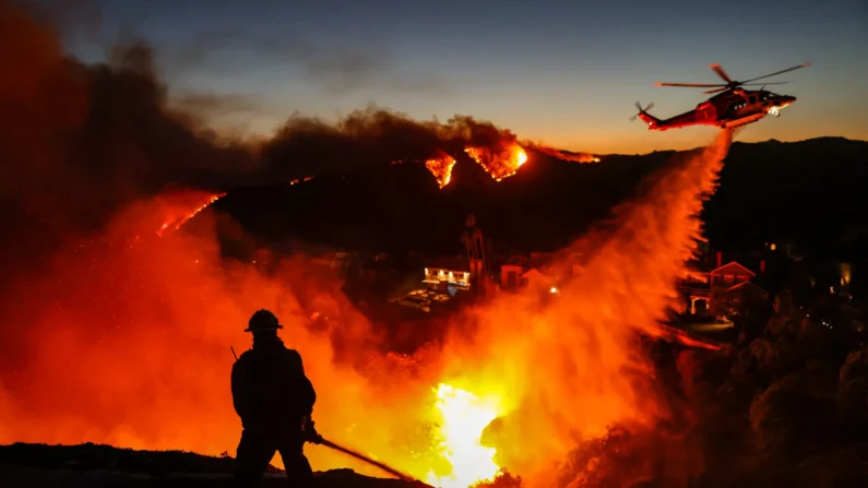 Un bombero enfrenta el fuego mientras un helicóptero lanza agua en el barrio de Pacific Palisades, en Los Ángeles, el 7 de enero de 2025. (David Swanson/AFP vía Getty Images)