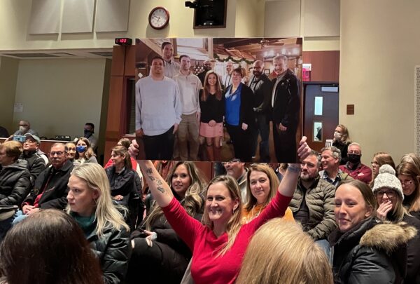 Un asistente sostiene una foto de grupo de miembros de la junta en la que todos fueron desenmascarados durante la reunión de la junta escolar del condado de Loudoun en Ashburn, Virginia, el 25 de enero de 2022. (Terri Wu/The Epoch Times)