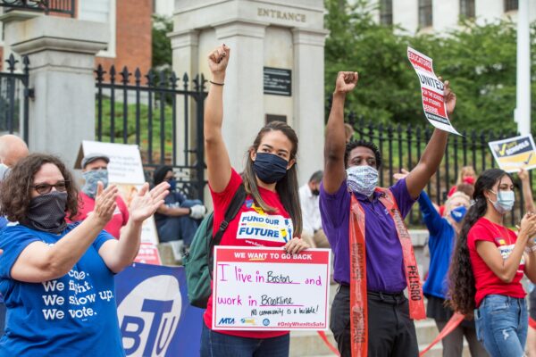 BOSTON, MA - AUGUST 19: People who are part of standout protest organized by the American Federation of Teachers chant, hold signs, and raise their fists outside of the Massachusetts State House on August 19, 2020 in Boston, Massachusetts. The group is calling for a uniform requirement for all districts to start the school year with a comprehensive distance learning plan as well as clear health and safety standards that must be met for the gradual return of in-person learning. 