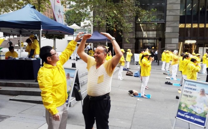 Un transeúnte se detiene para aprender los ejercicios de Falun Dafa durante la práctica de grupo en Australia en esta foto de archivo . ( Minghui.org )