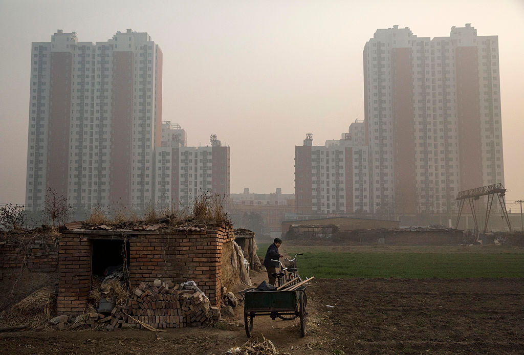 Un granjero chino se encuentra fuera de su casa. Al fondo una nueva urbanización en Hebei el 21 de noviembre de 2014. (Kevin Frayer / Getty Images)