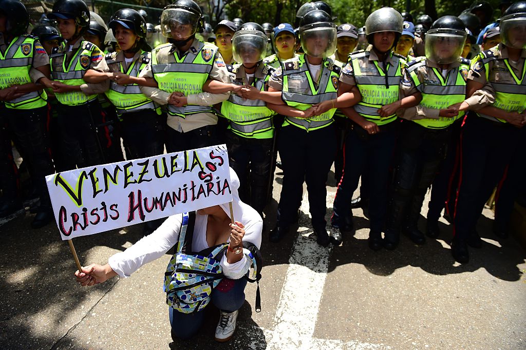 Una manifestante sostiene un cartel que dice 'Venezuela crisis humanitaria SOS', mientras la policía monta guardia en una manifestación contra las políticas del gobierno del presidente Nicolas Maduro en Caracas el 26 de mayo de 2016. (RONALDO SCHEMIDT/AFP/Getty Images)